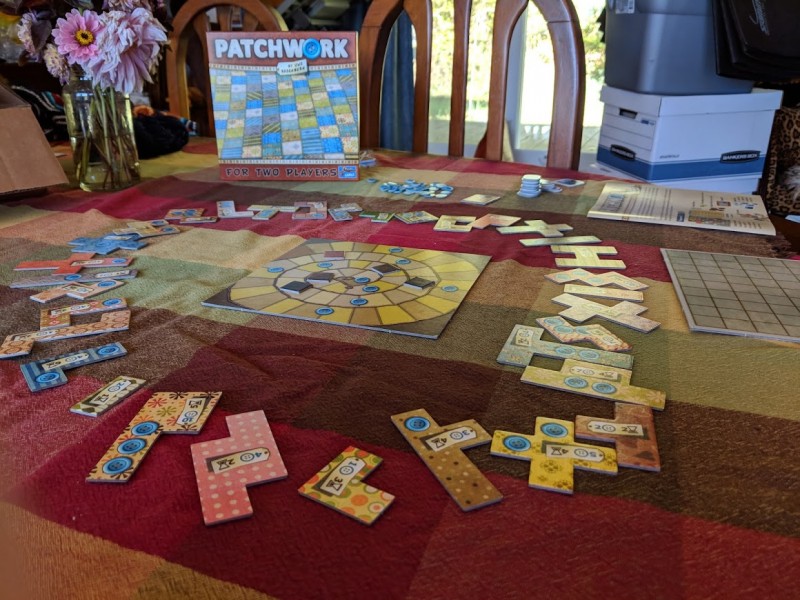The game Patchwork set up and ready for play, with a square board that keeps track of player turns and differently shaped pieces of various colors representing quilt patches surrounding the board.