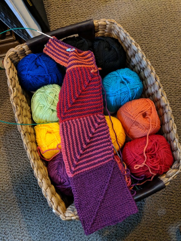 Three and a half squares of the Hue Shift afghan, laying atop a basket of yarn.