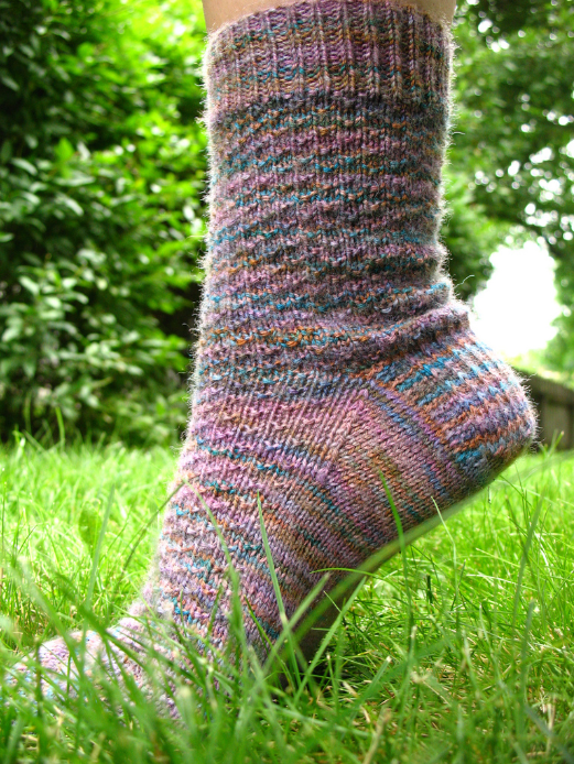 A foot on tiptoe in the grass, showing off a sock made from the Hermione's Everyday Sock pattern