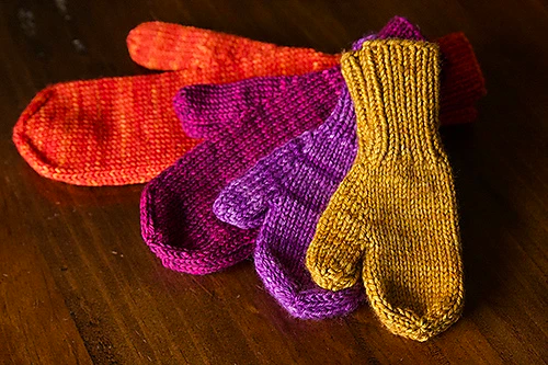 A set of four knit mittens in different sizes and colors.
