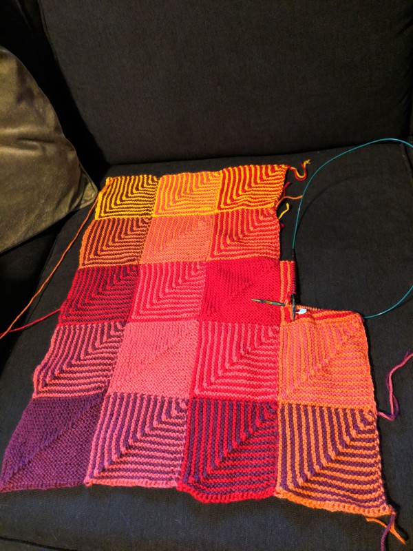 Part of an afghan, in shades of red, pink, yellow, and orange.