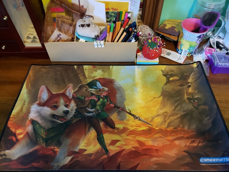 A Magic playmat with a corgi and a faerie about to fight some angry raccoons on it.