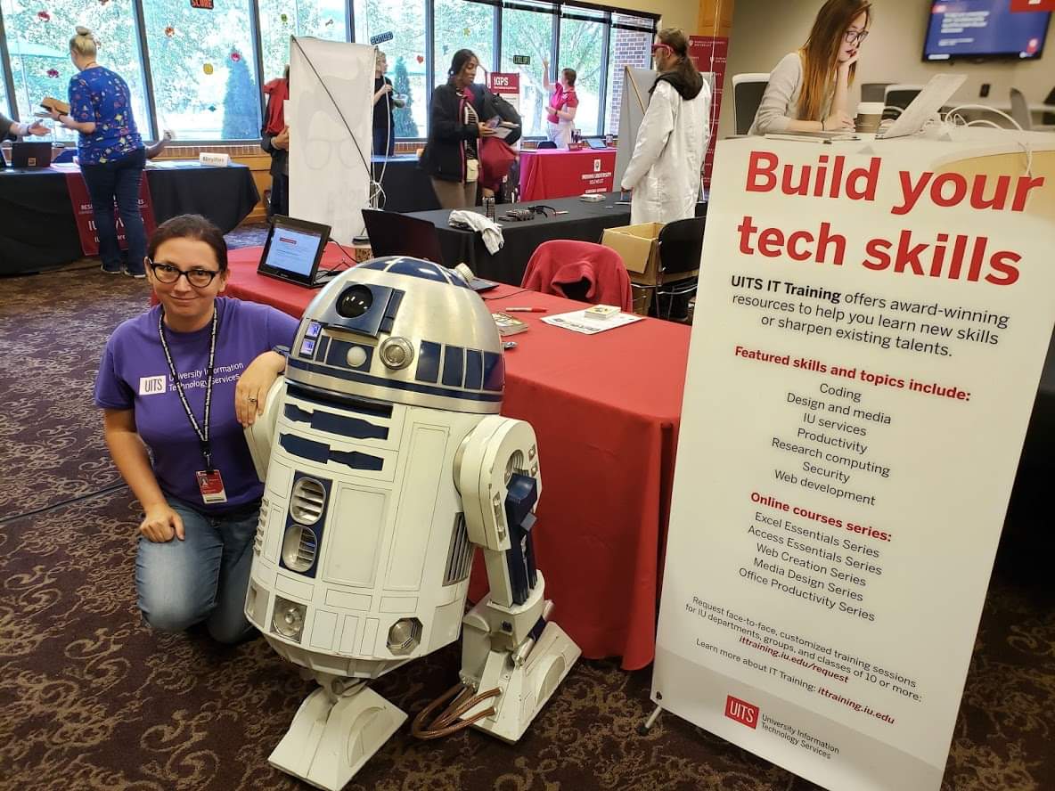 Me kneeling next to a remote-controlled R2-D2 in front of IT Training's booth at Game On. 