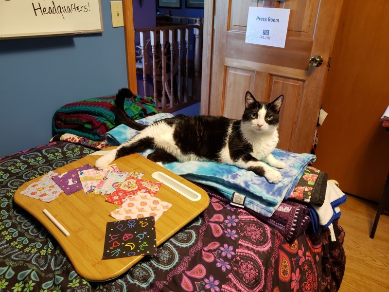 A tuxedo cat laying on a bed in front of a lap desk with fabric squares on top of it.