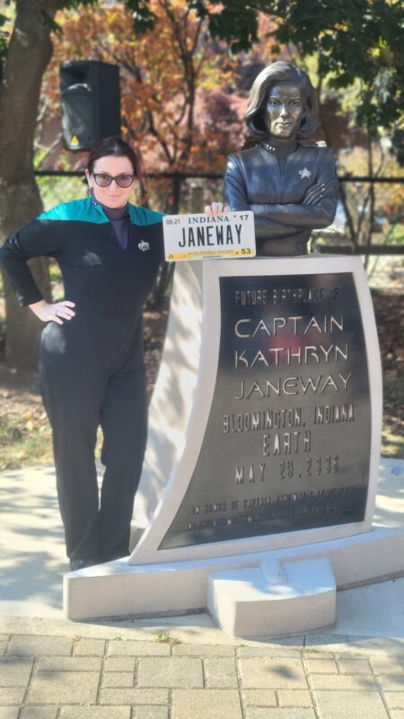 Me in my Starfleet science officer uniform, standing next to the Captain Janeway statue in Bloomington, IN. I'm holding my Janeway vanity plate up in front of the statue.